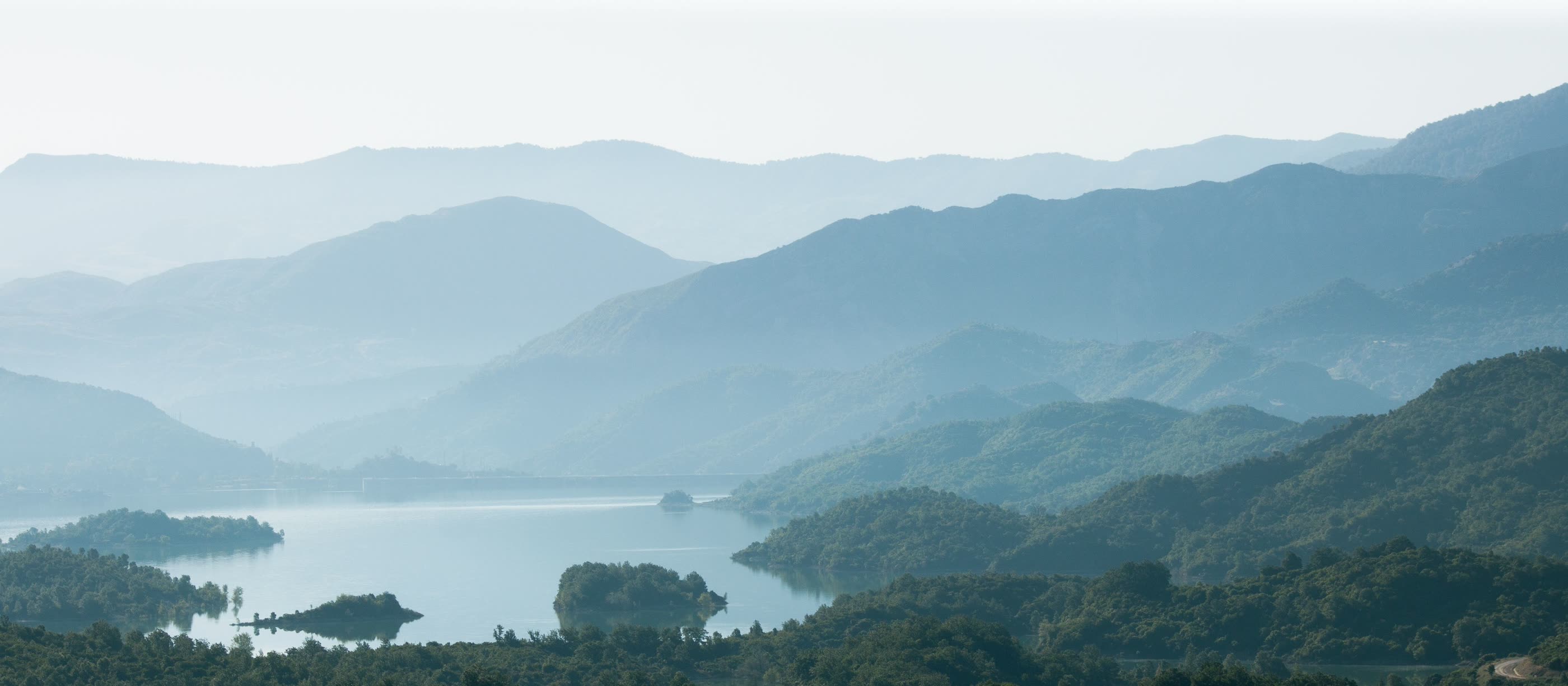 Layered mountain ridges fading into haze above a still lake