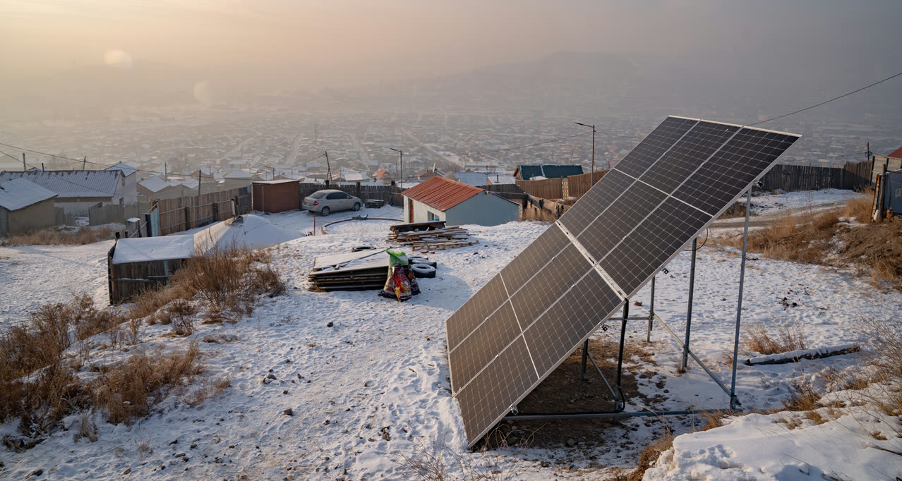 A solar panel on a snowy hillside above a city under haze